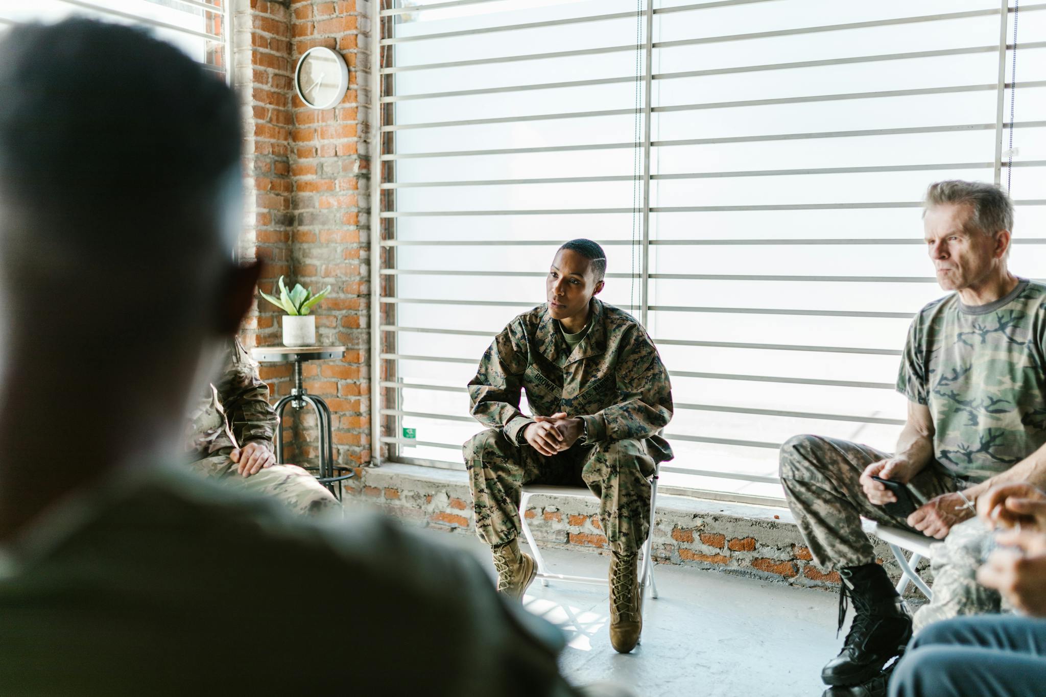 Military personnel participate in a supportive group therapy session indoors.